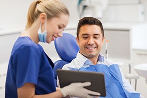 Patient smiling while dentist assistant reviewing information on tablet